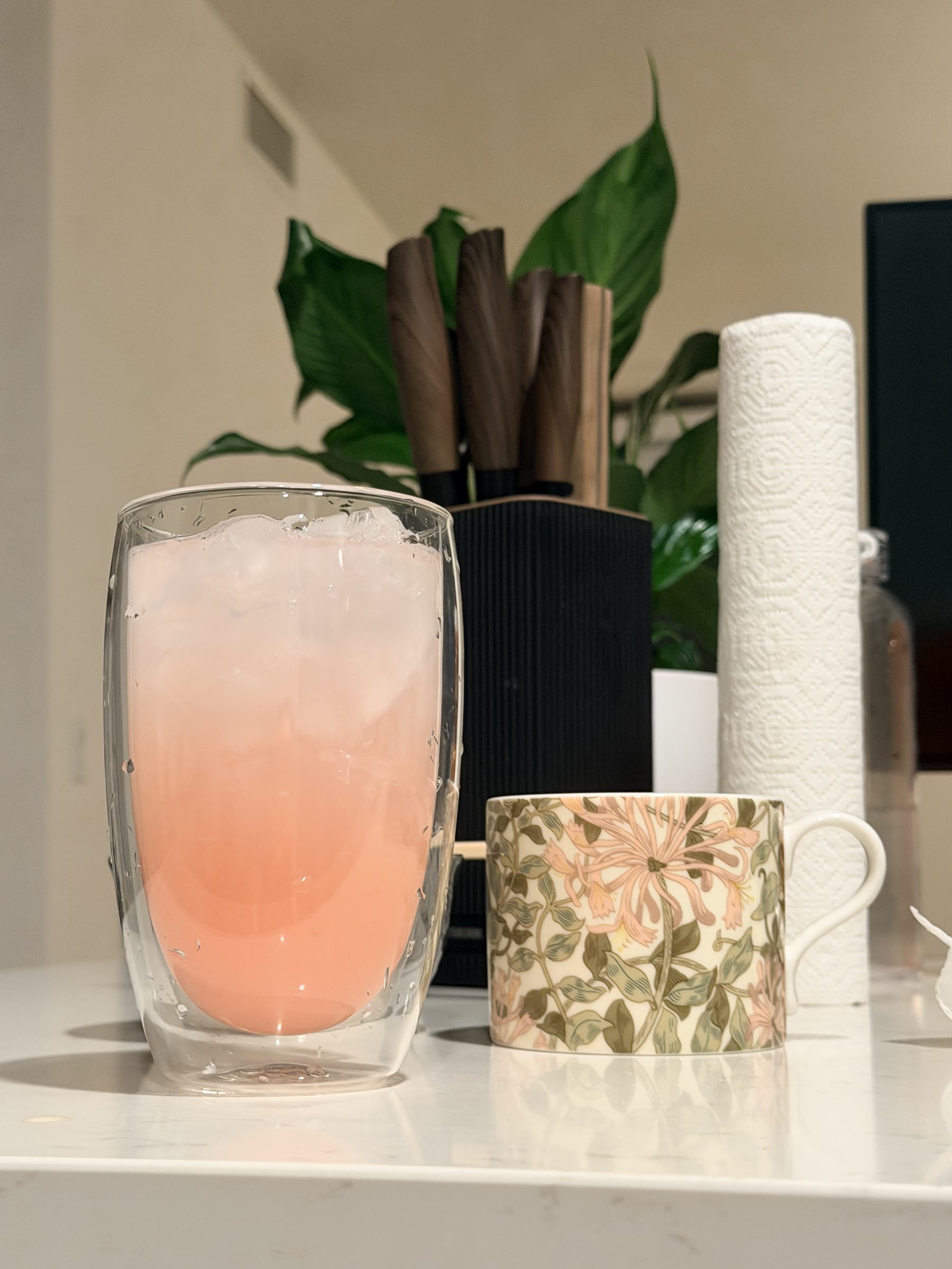 A pink iced drink beside a floral mug