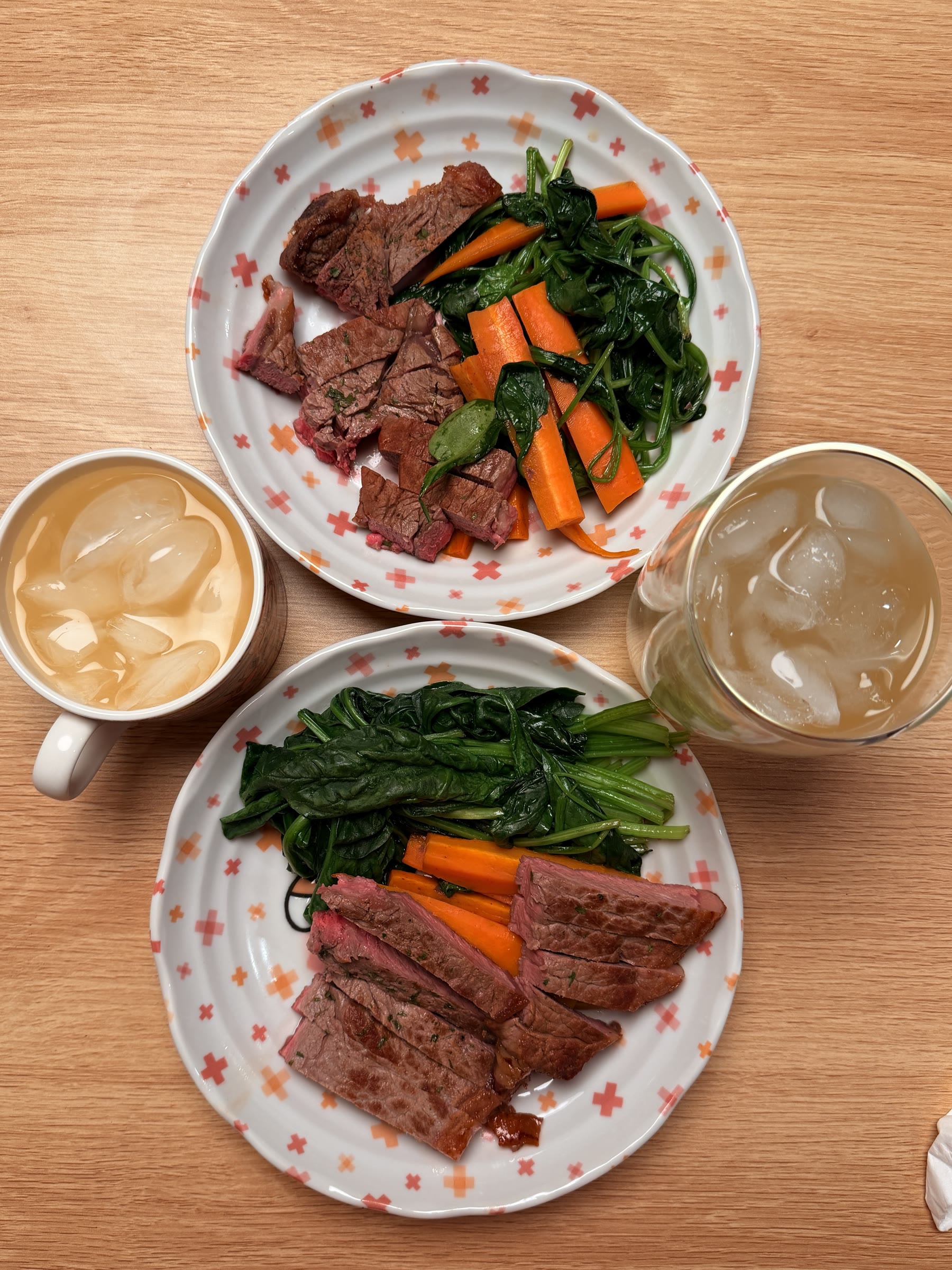 Two steak dinners with spinach, carrots, and iced drinks
